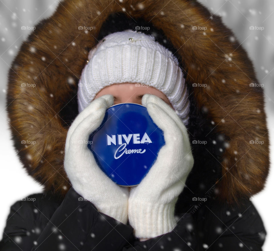Young woman holds a Nivea cream in front of it self in the snowfall.