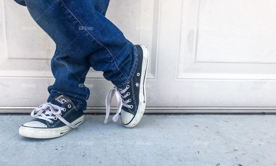 Boy in blue jeans and converse style shoes stand with foot crossed