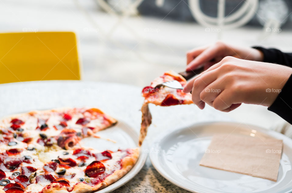 Girl's hands taking a slice of pepperoni pizza in a cafe.
