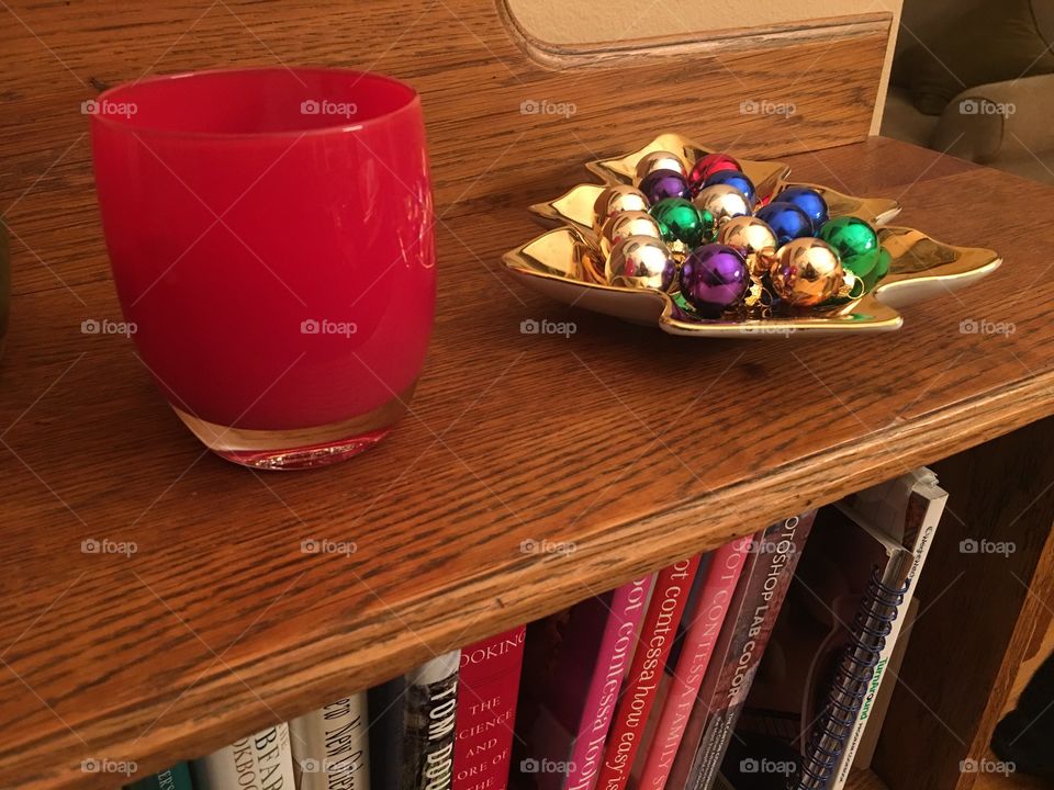 Red Glassybaby votive on shelf next to golden tray of miniature Christmas ornaments 