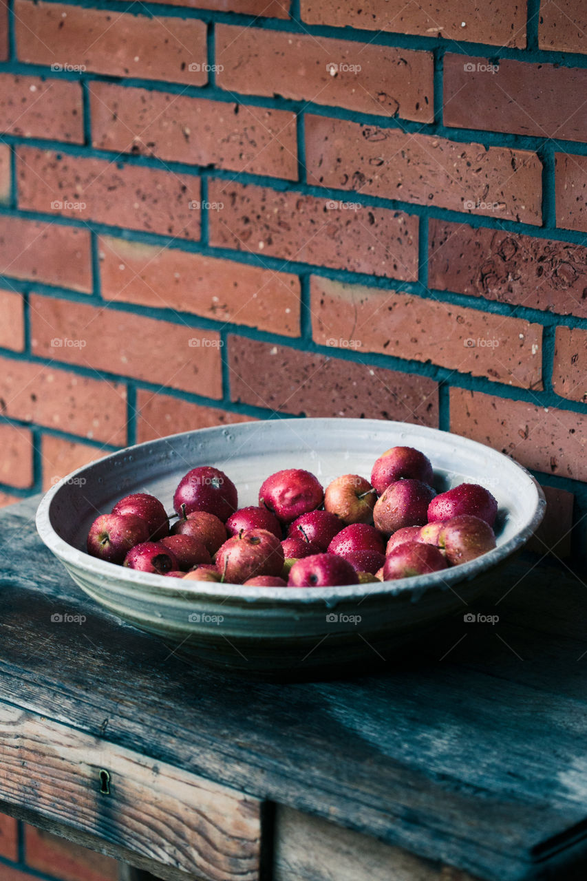 Closeup of big bowl of fresh red apples sprinkled raindrops on wooden table