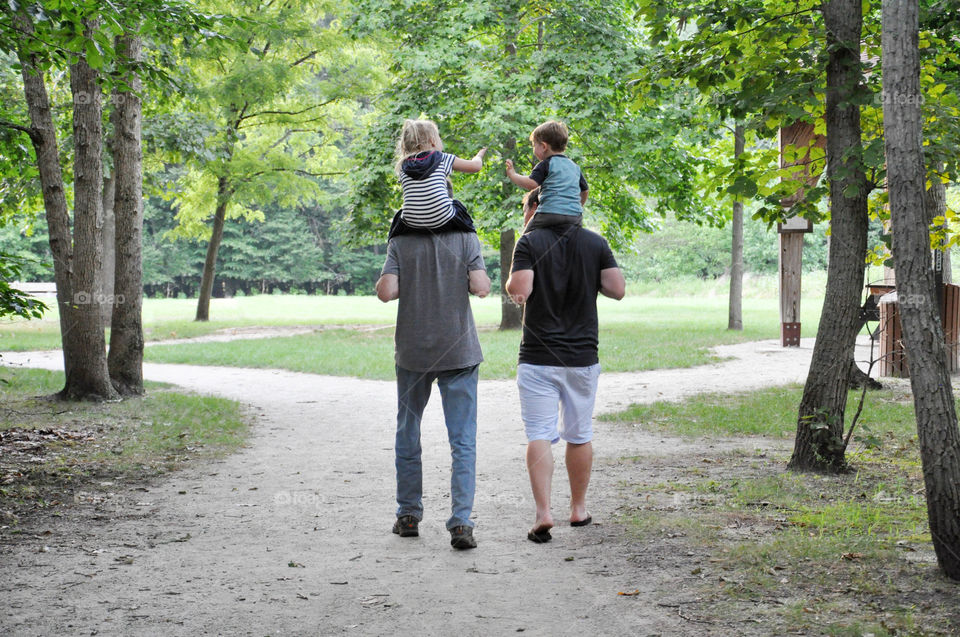 Two dads are seen walking together with their children on their shoulders