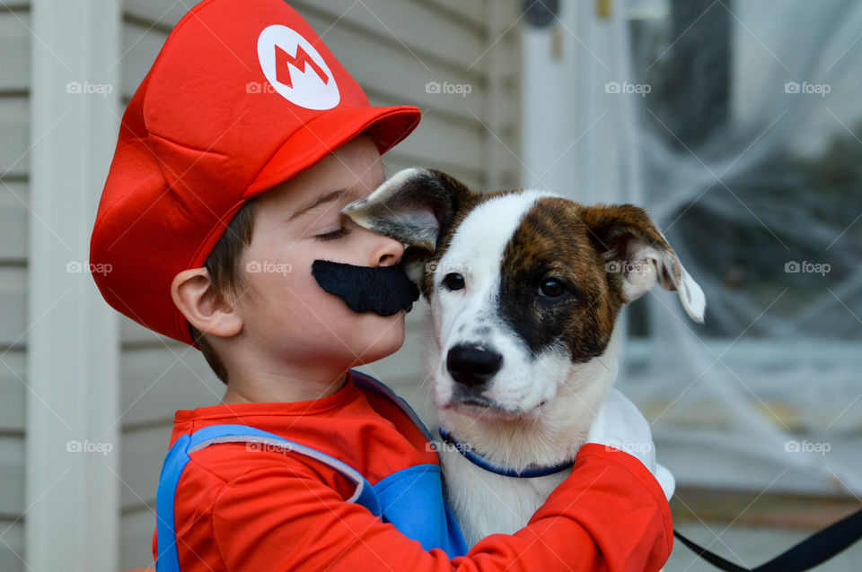 Young boy dressed in a Mario Halloween costume and giving his dog a kiss