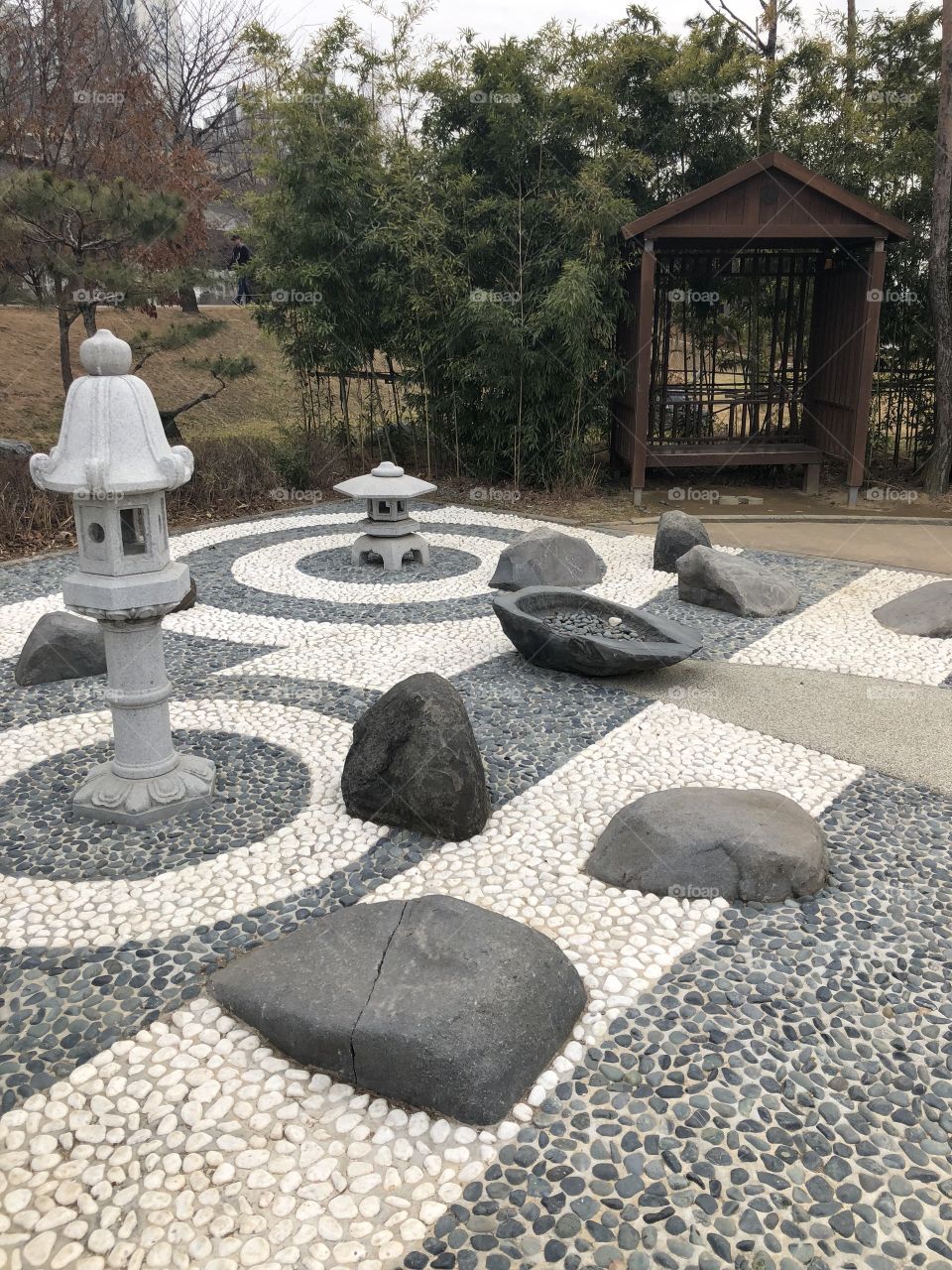 A geometric and peaceful zen garden in the middle of a quiet park featuring boulders and pagodas and a small sitting area to reflect. 