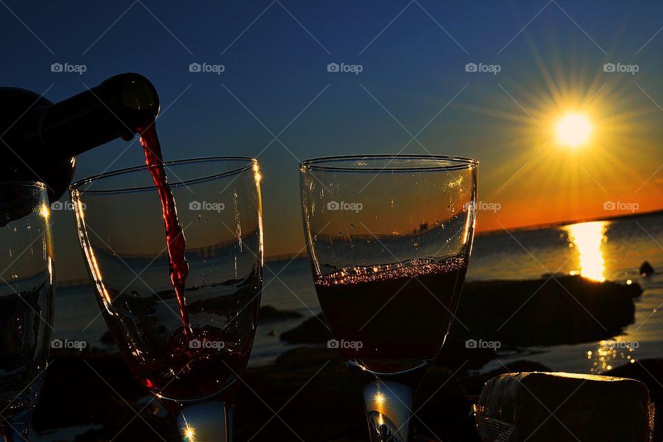 Wine glow at sunset on ocean. Pouring wine into glasses at sunset, viewing through the glasses