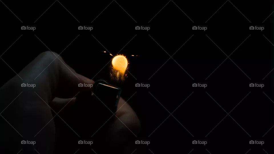 A person has lighters in his hands and he lights it through a flint wheel, the lighter ignites, sparks and fire appear, close-up on a black background.