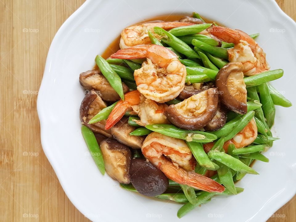 Healthy food stir-fried string bean with shrimp and shiitake mushrooms in white plate on dining table - top view