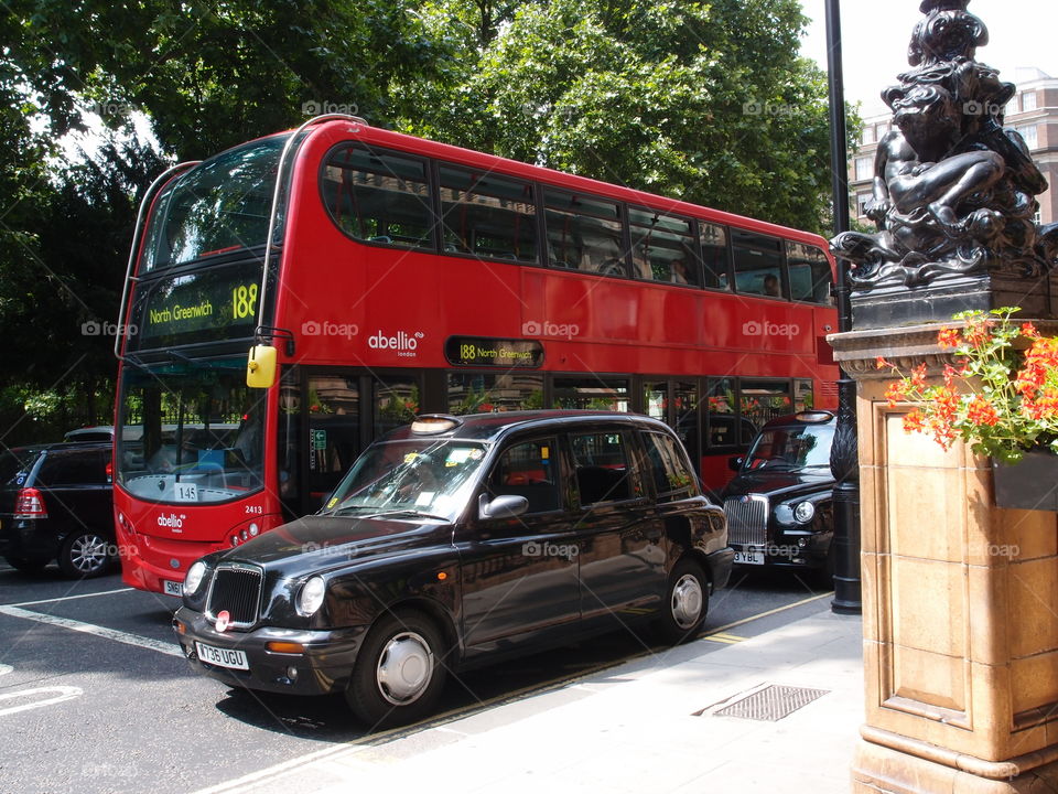 A small black car with a brilliant red double-decker bus on the busy streets of London on a beautiful sunny summer day. 