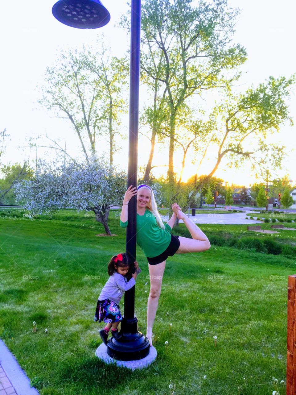 mother practicing yoga poses in the park with her young daughter.
surrounded by lush green grass and trees and flowers