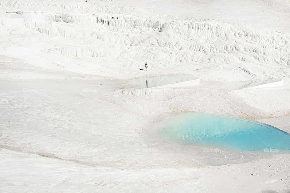 Tiny human standing on a white chalk surface of a mountain with small blue lagoons