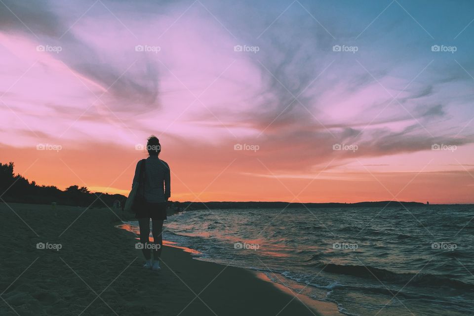 A woman walking alone on the beach at sunset