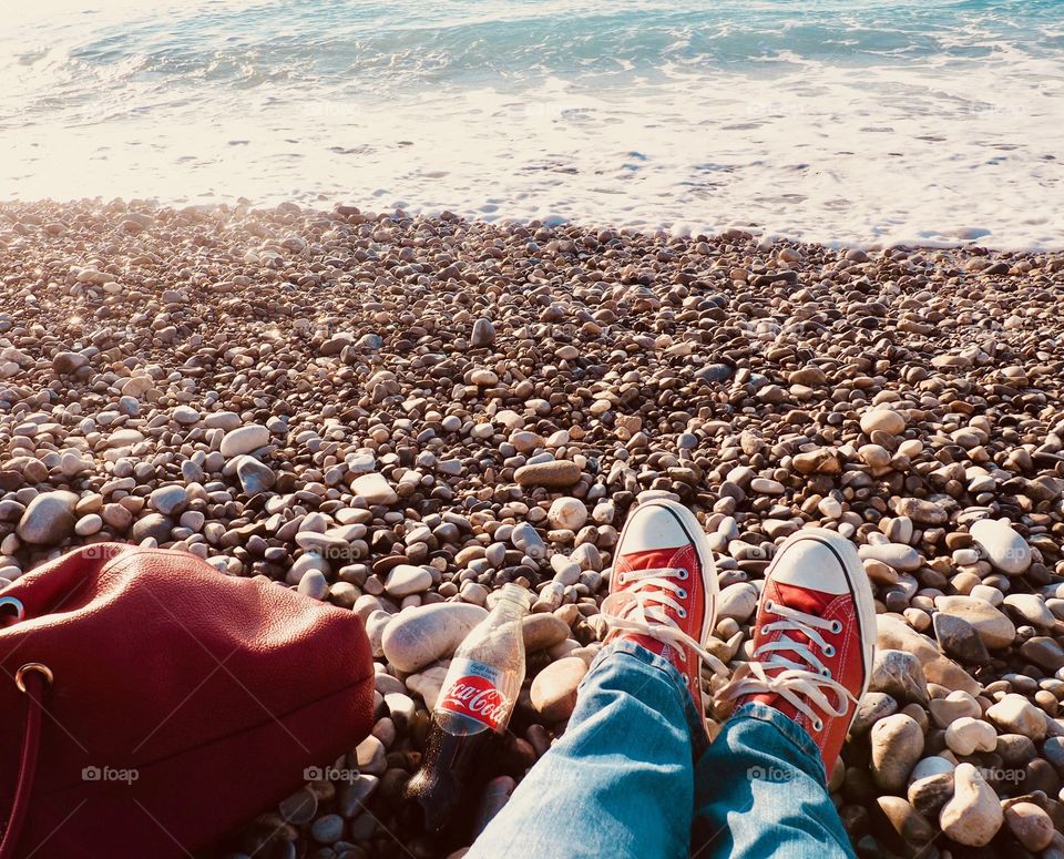 A bottle of Diet Coke on the beach with red sneakers and red leather bag.