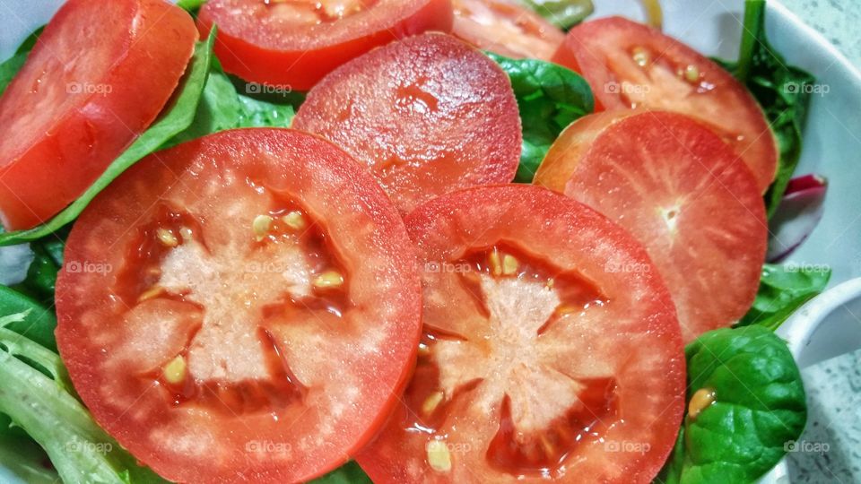 Sliced tomatoes on top of green leafy vegetables make up for a freshly prepared salad meal.