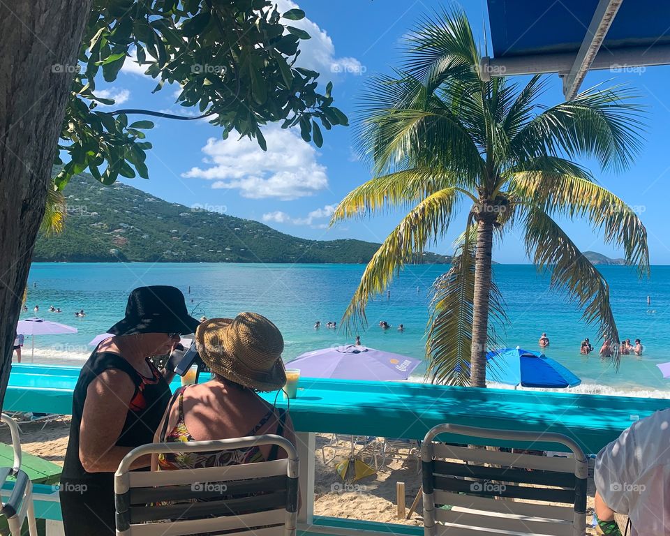 People on the beach with palm trees sitting on chairs water and mountain background