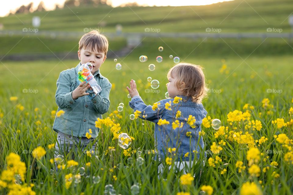 A boy and a girl play with a gun with soap bubbles