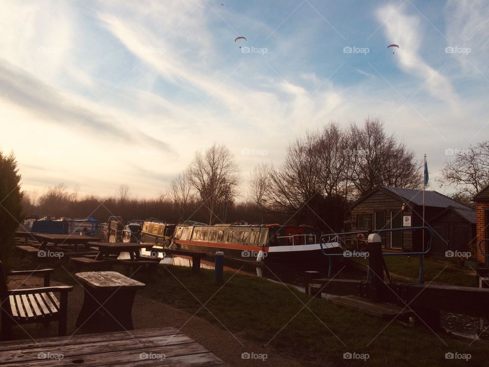 Paragliders over canal, houseboats and trees in winter sunlight British sunset sky