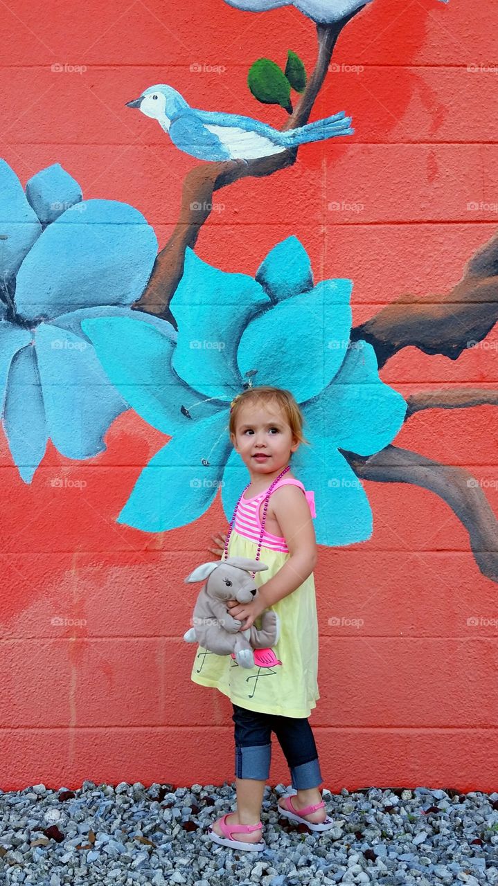 Cute girl standing against painting wall