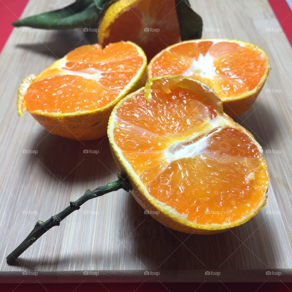 Halves of fresh juicy mandarin oranges with twig and leaves on a cutting board