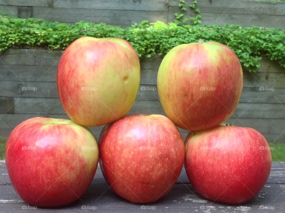 Apples stacked outdoors on wooden bench.