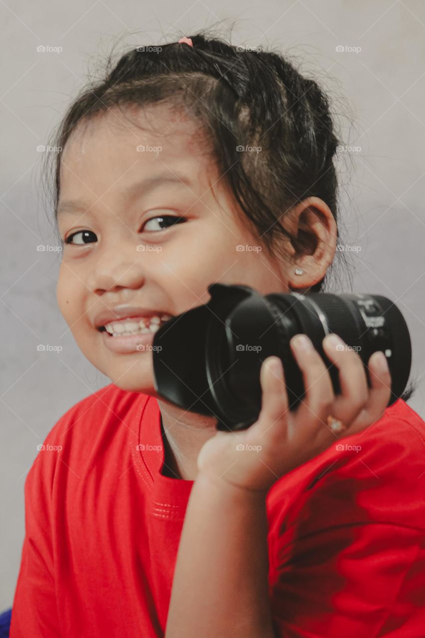 Portrait of a little girl holding a camera lens