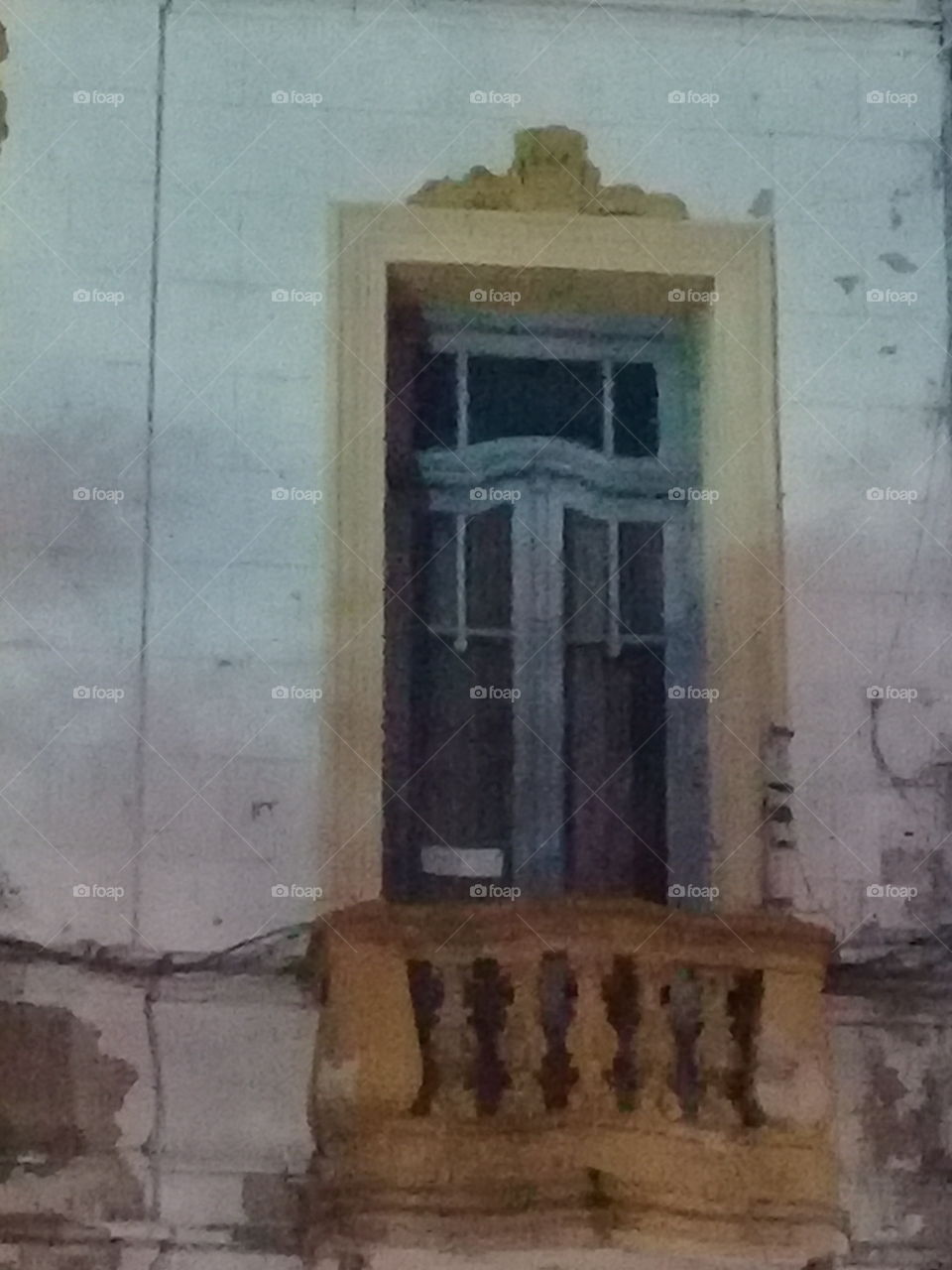 centenaria ventana con balcón y antigua celosía de madera entrecerrada, pintada de amarillo y verde.
