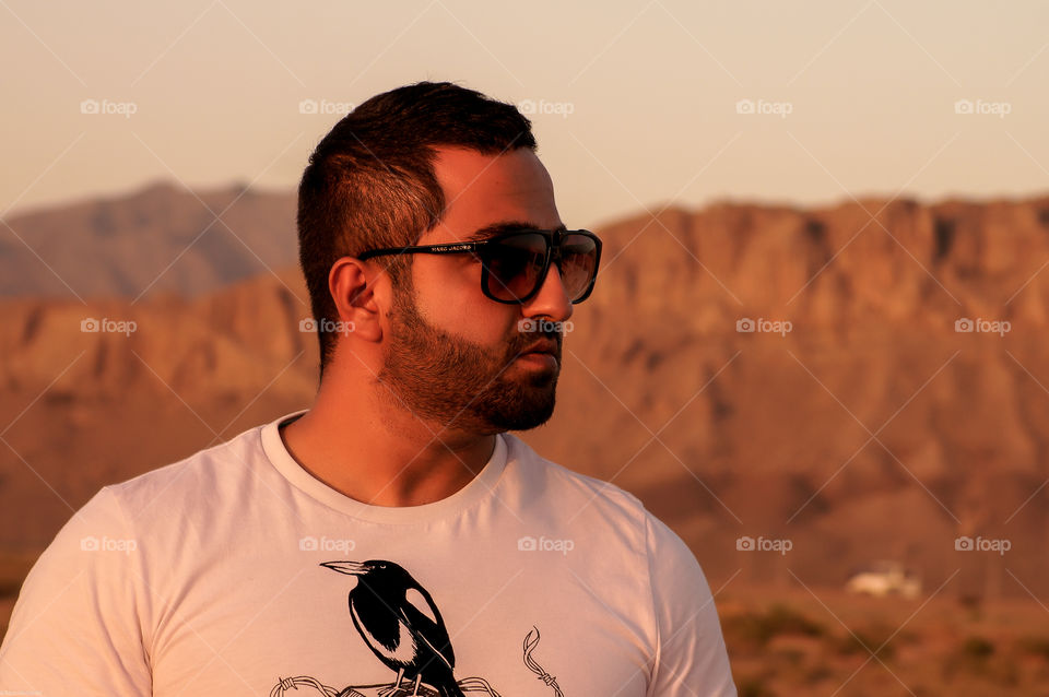 Desert Style. A handsome guy in the sunset in a desert with red mountains wearing an stylish sunglasses and looking afar