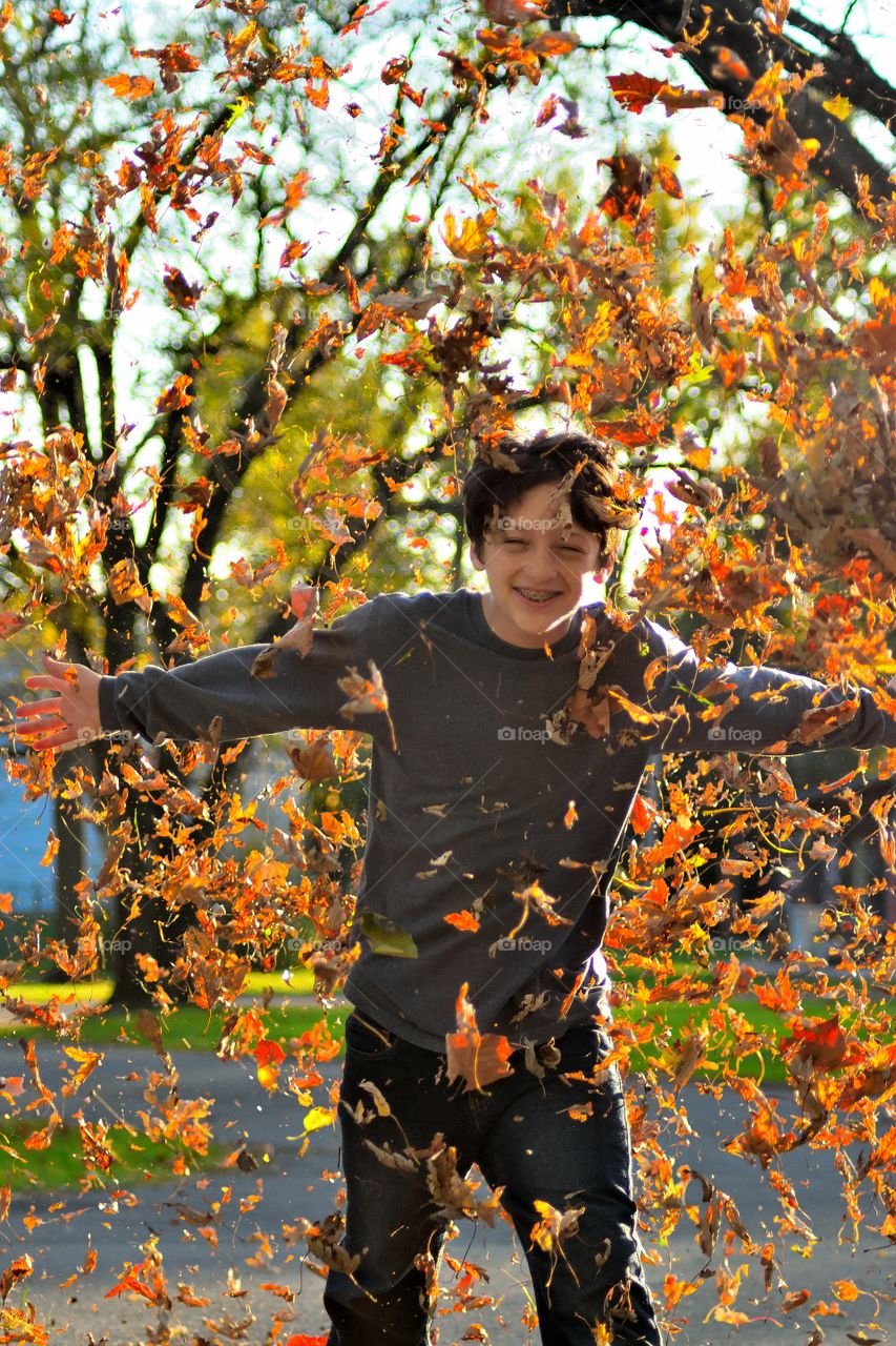 Portrait of a happy boy with falling autumn leaves