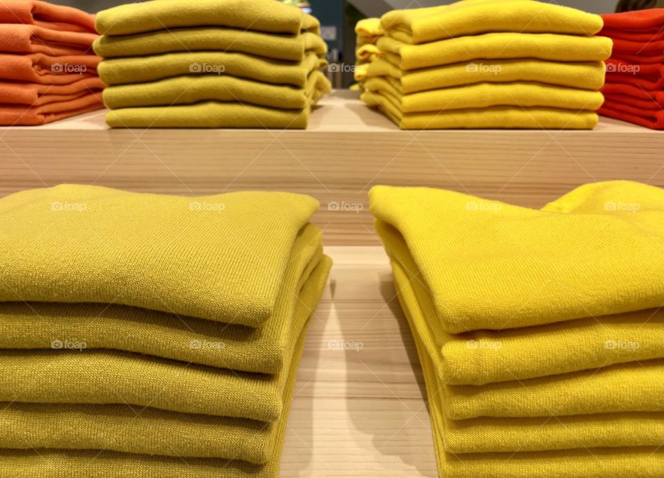 Series of yellow folded sweaters on wooden shelves, piles of wool sweaters 