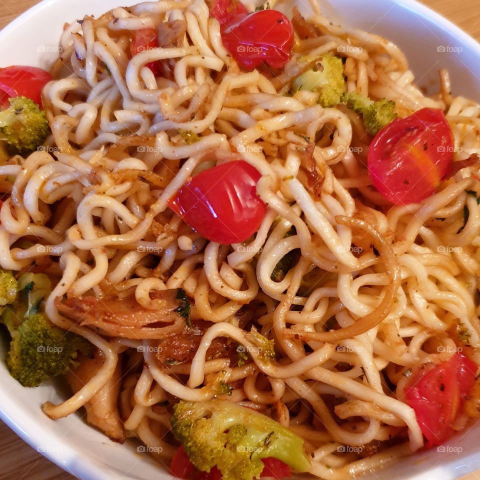 Fried noodles with tomatoes and broccoli in a bowl.