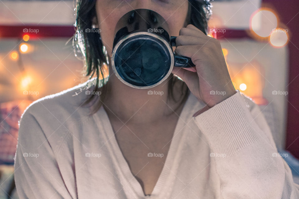 Girl drinking coffee in a black mug with lights on behind