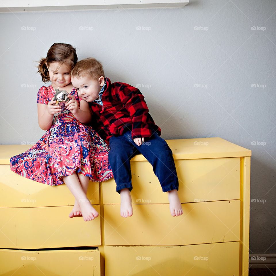 Two kids sitting on a yellow dresser