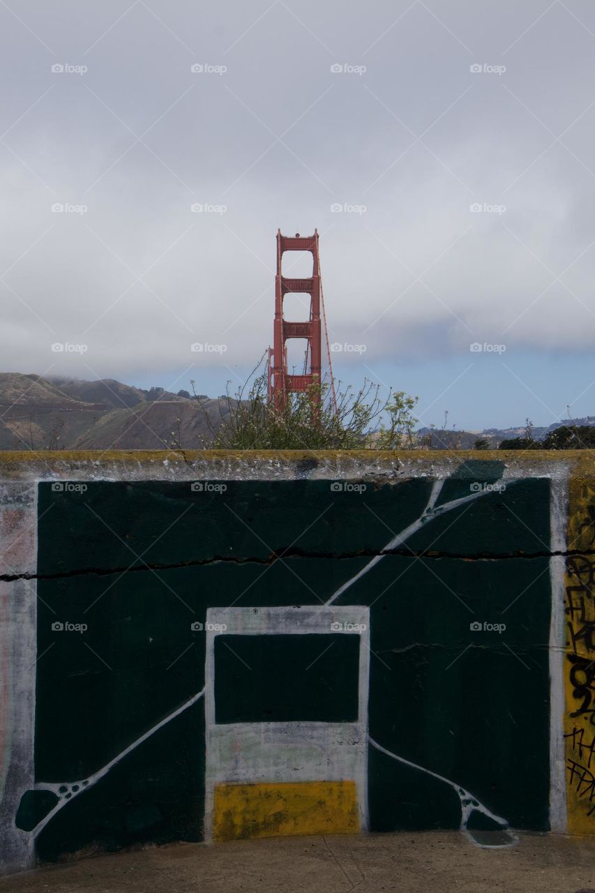 Golden Gate Bridge towering above the old military barracks at the Golden Gate viewing point in San Francisco California with the contrast of graffiti on the old cement walls