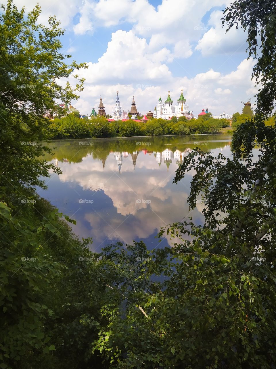 Summer landscape.  Exit andforests to the river bank, on the opposite side of the dome of the towers.  Reflection in water of trees, towers and sky with clouds