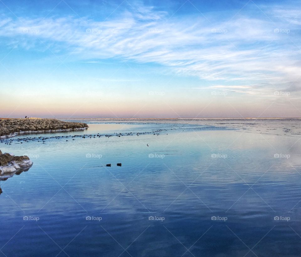 Pastel blue sky and light clouds reflecting in the calm waters of Lake Michigan 
