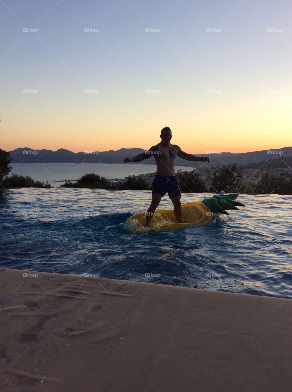 Man standing on a lilo in a infinity pool with a stunning background