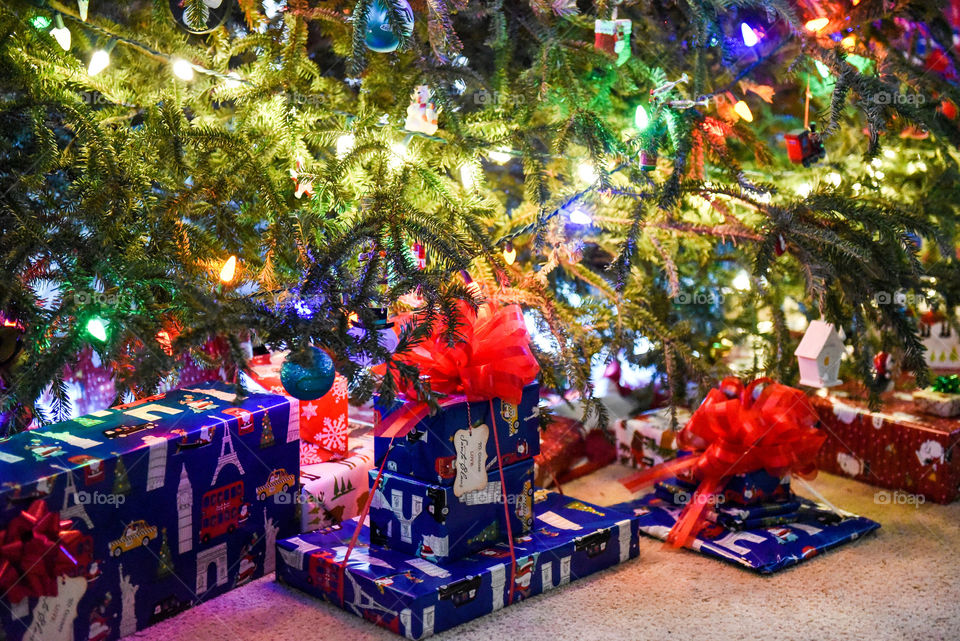 Wrapped presents under an illuminated Christmas tree at night indoors