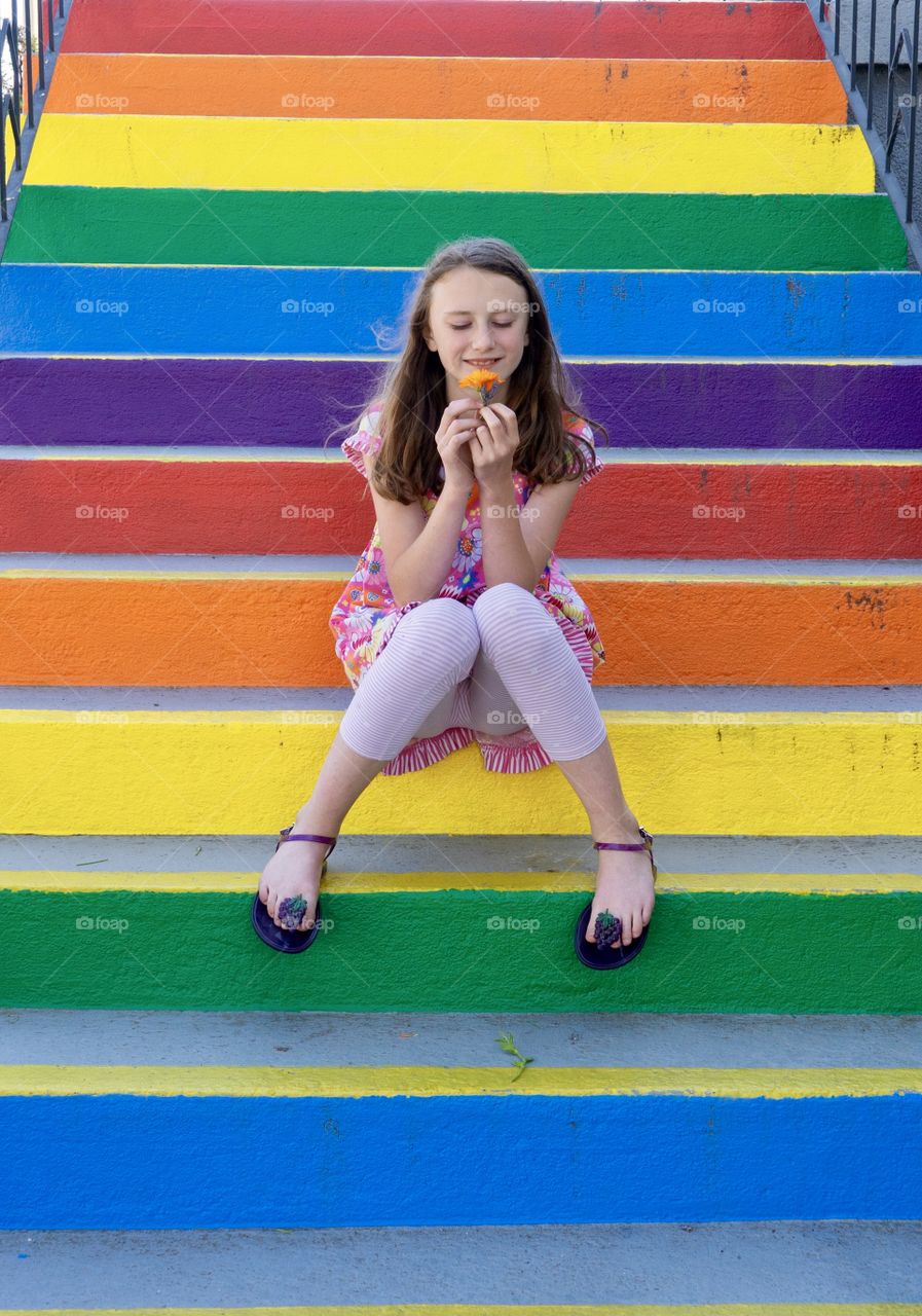 Girl smells orange flower on bright multi-coloured stairs