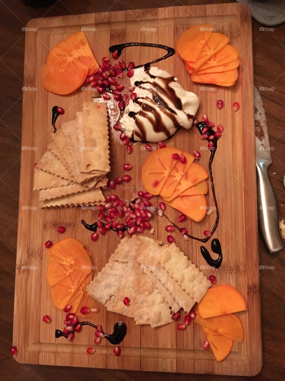 Cheese plate with burrata, pomegranate, persimmon, and a balsamic drizzle spread out on a wooden platter
