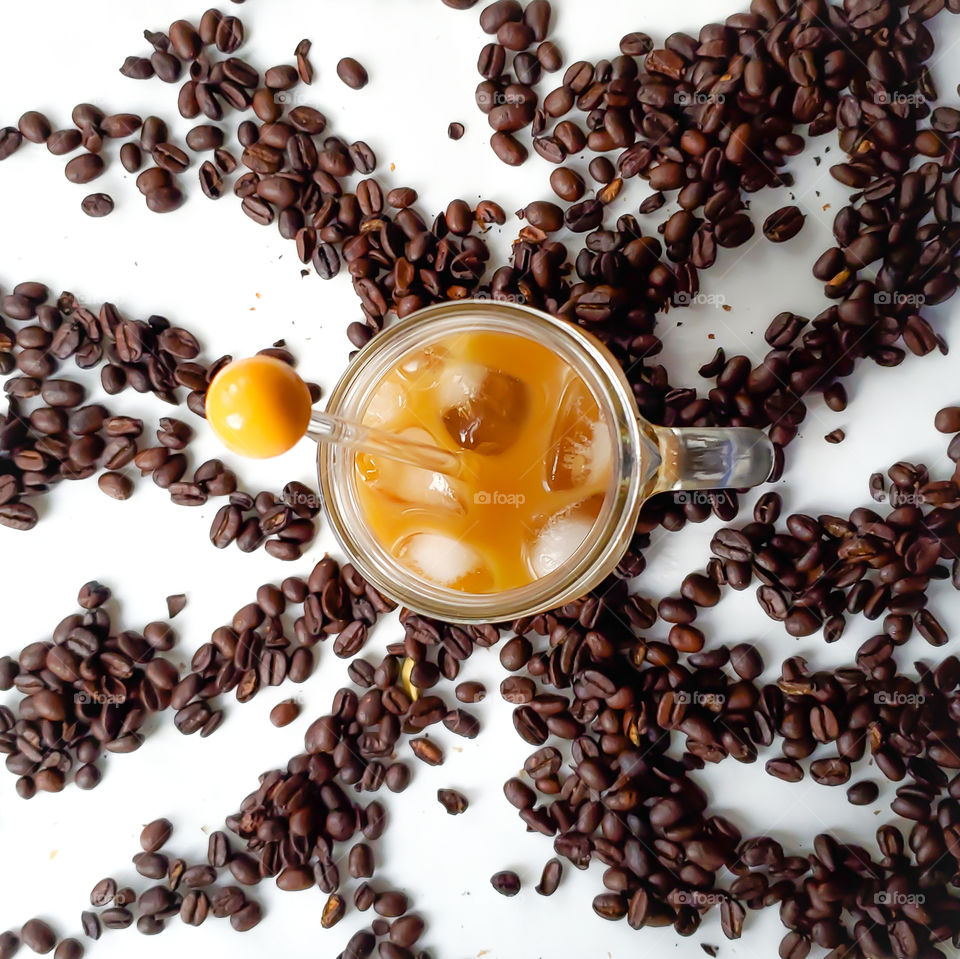 Cold brew ice coffee at hom. With almond creamer in a mason jar with a handle. On a white background surrounded by organic whole coffee beans.