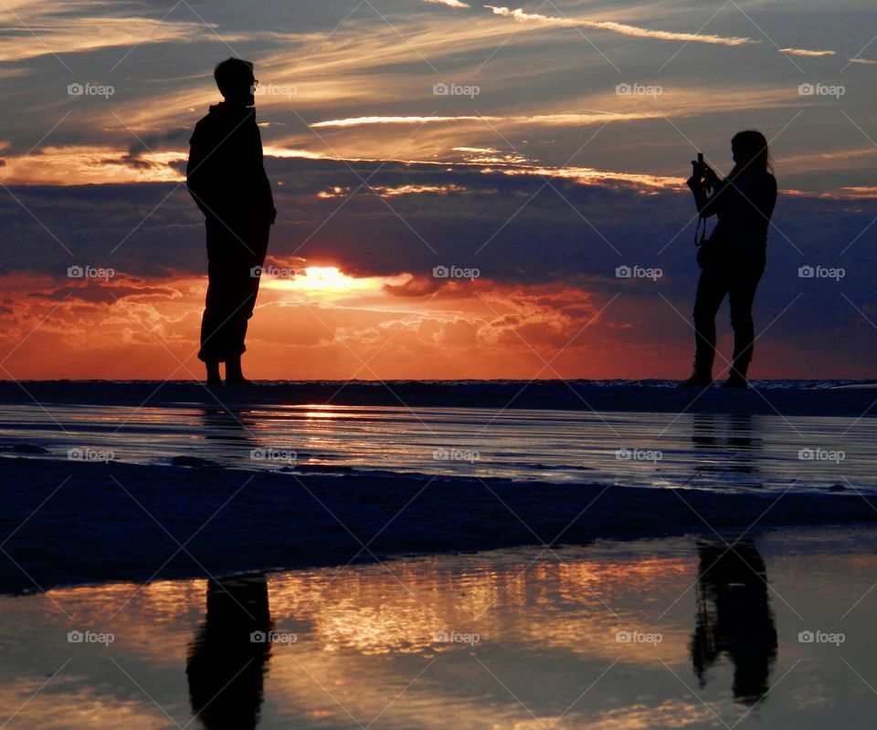 Silhouettes and shadows - A couple take photos in front of the Gulf of Mexico during a spectacular and colorful sunset 