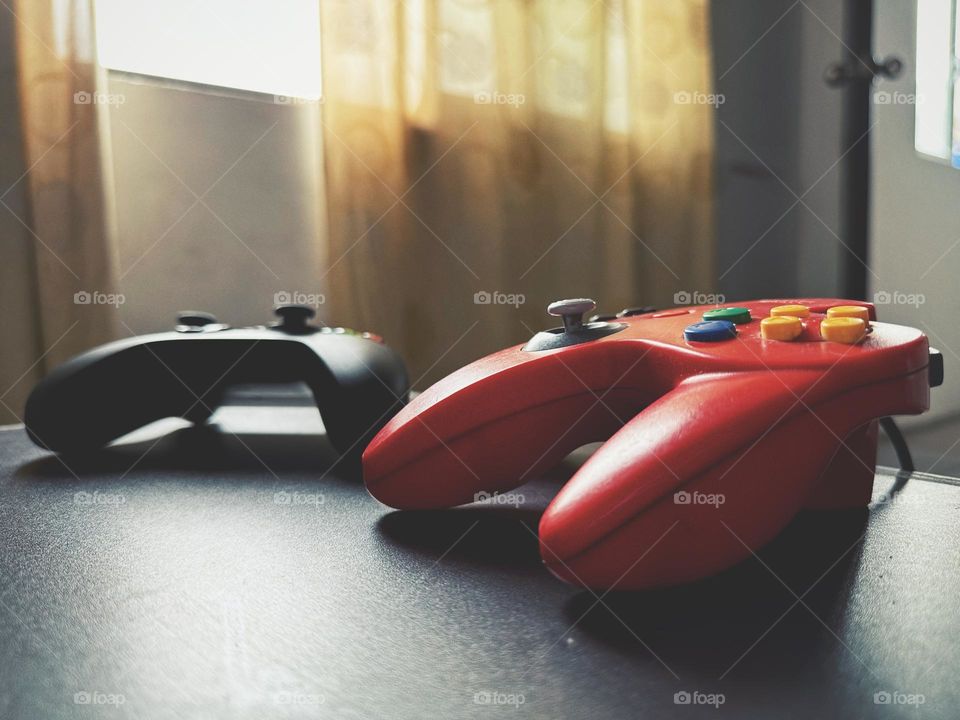 Xbox and Nintendo controllers situated on a wood table, while the natural light enters through the window.