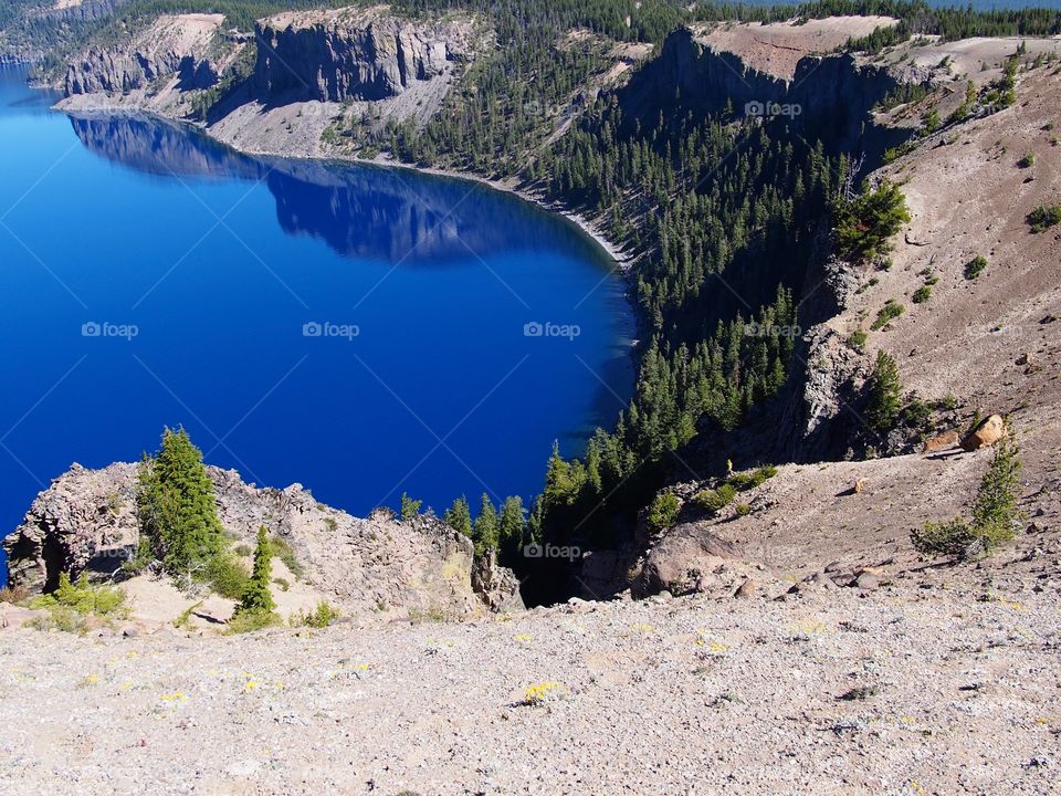 The rugged rim reflect in the stunning rich blue waters of Crater Lake in Southern Oregon on beautiful sunny summer morning. 