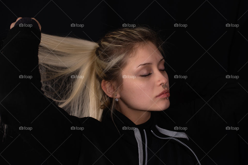 portrait of beautiful blonde woman taking her hair with eyes closed black background
