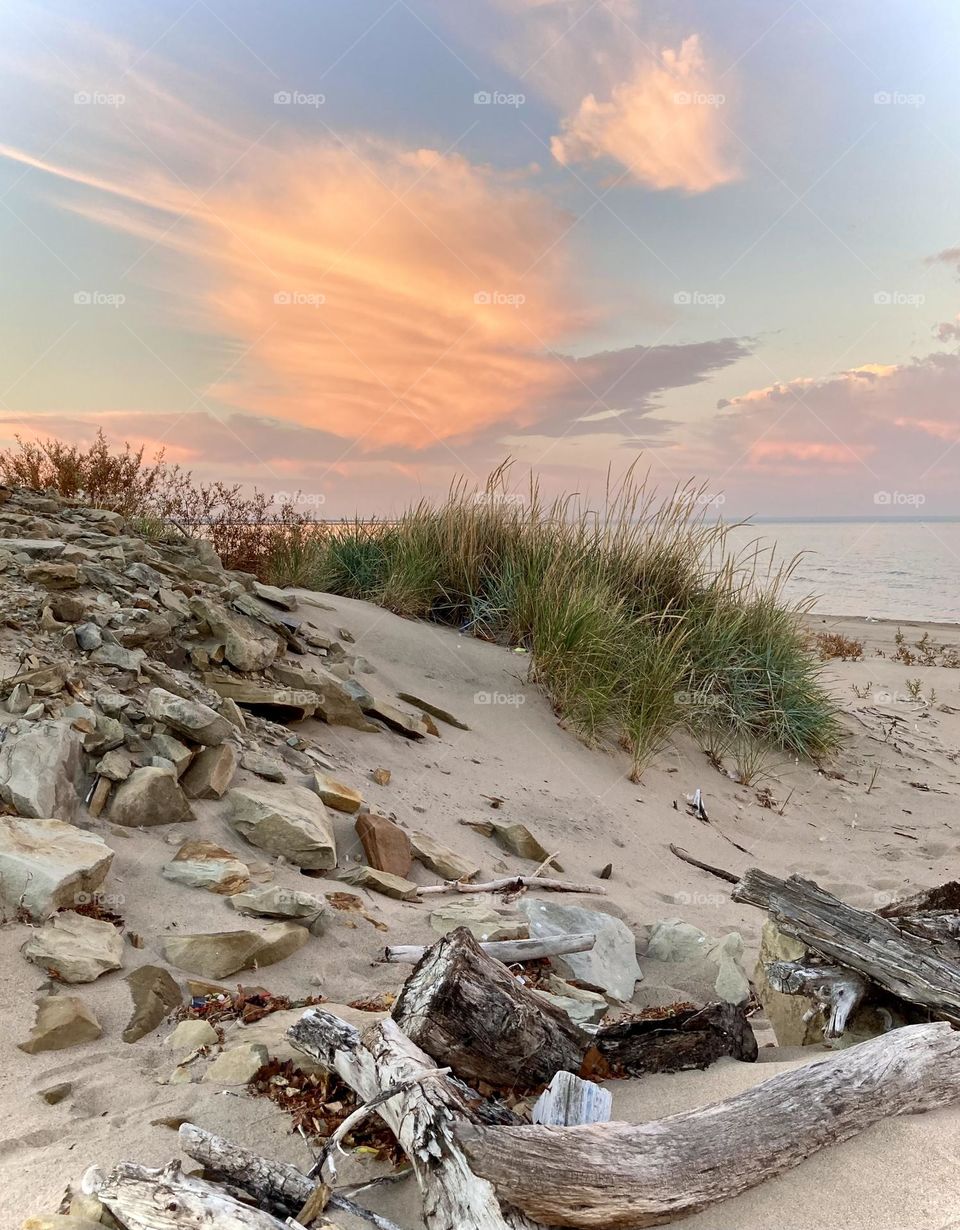 Pink and purple sunset on lake eerie shoreline on Cedar Point’s sandy, rocky beach with beach grass in foreground