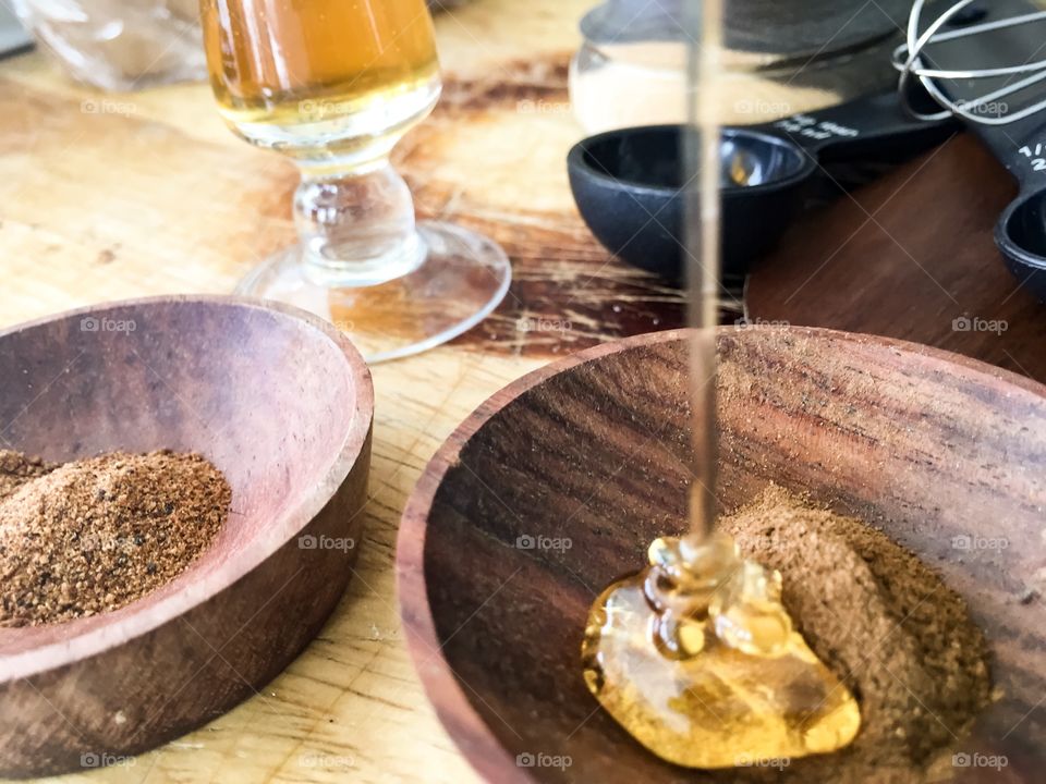 Making natural chai facial mask for weekly beauty routine pouring honey onto cinnamon with nutmeg in bowl measuring spoons and mini wire whisk on the table 