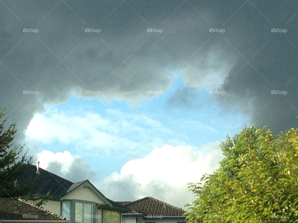 Housing Market Boom or Bust?. Blue portal through dark clouds over homes on hill