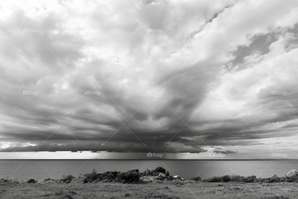 People watching a storm over the ocean approaching the coast, big cloud formation , b&w