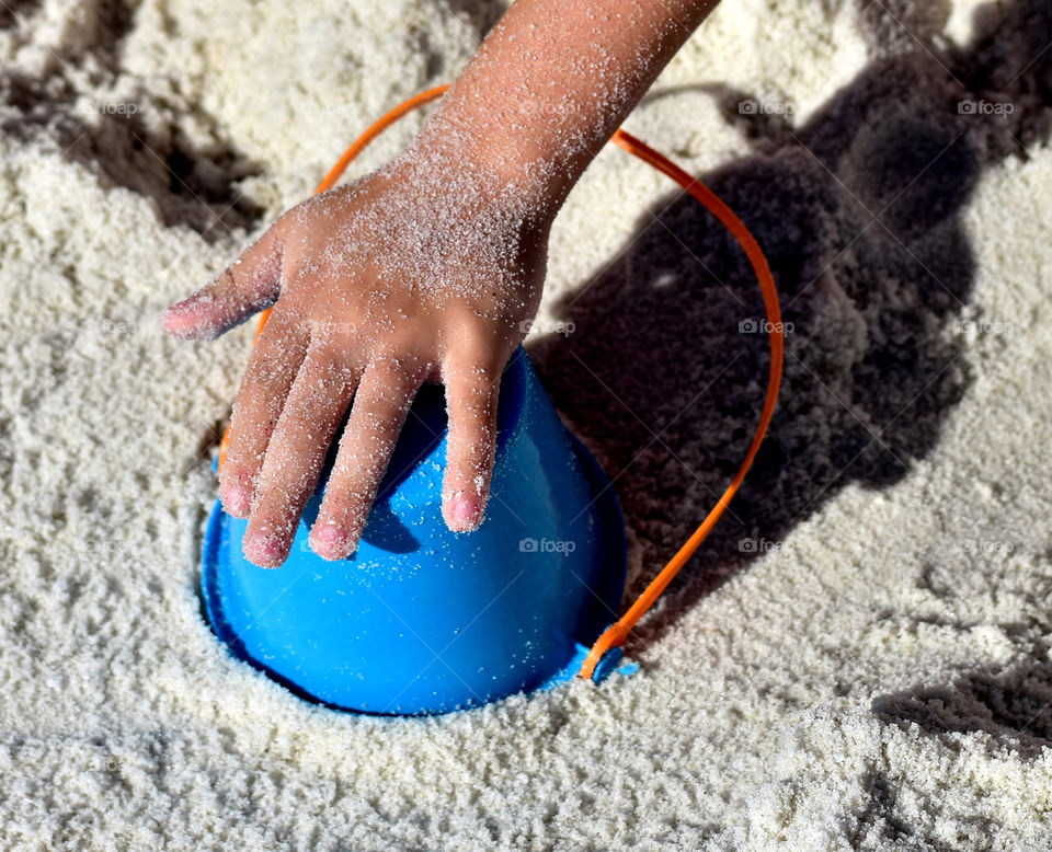 Hand holding bucket in sand at beach