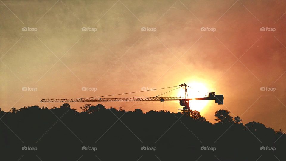Silhouette of a hilly forest landscape and an abandoned construction crane against the sunset 