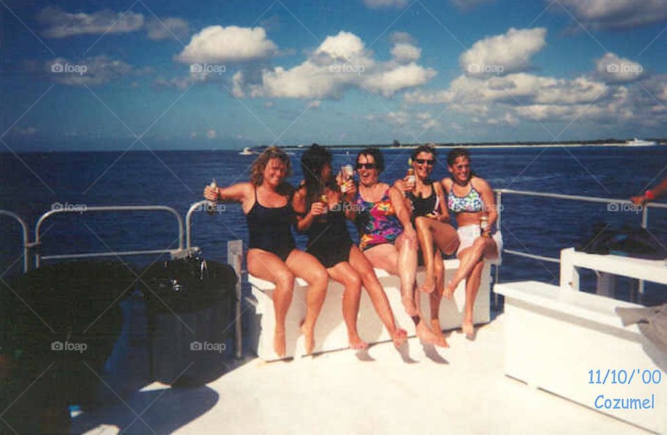 Girls having fun on back of boat deck out on ocean. They're all laughing, partying and having fun. All are wearing bathing suits.